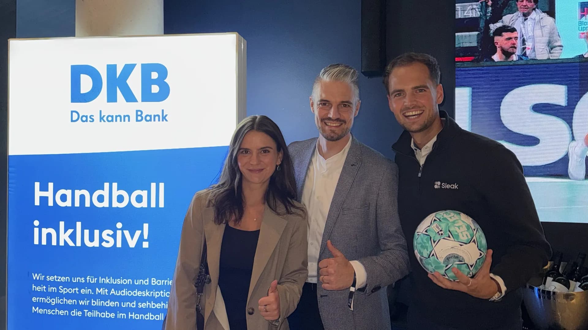 Das Sleak-Team mit einem Gastgeber der DKB vor einem Handball-Rollup beim Rexel Super Cup 2026